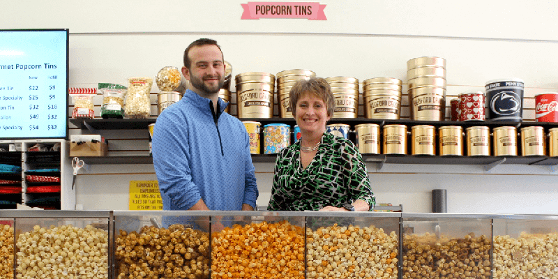 Bedford Candies owners smiling with a mouthwatering candy treats behind a retail counter