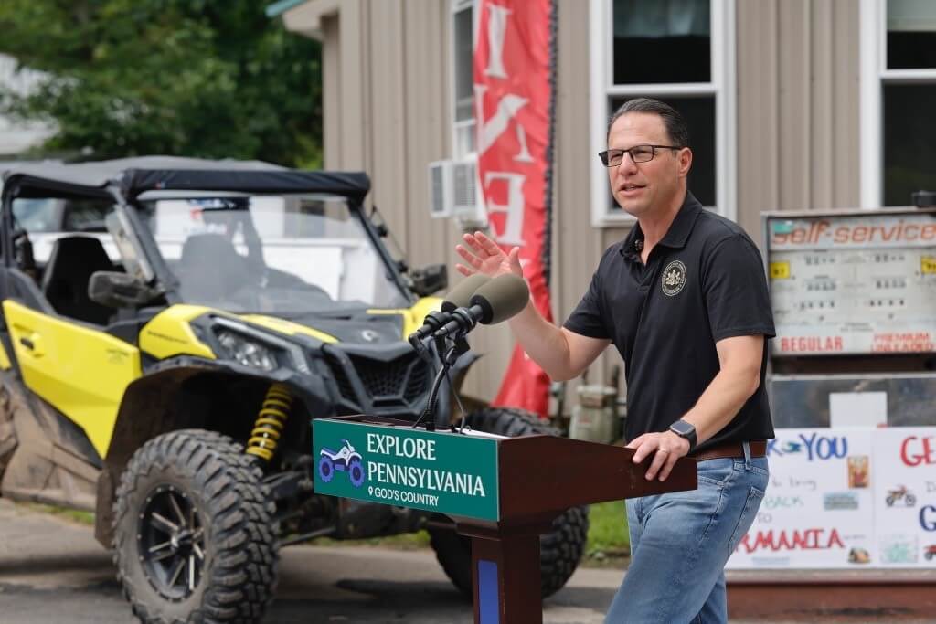 Governor Josh Shapiro at a podium announcing that the Department of Community and Economic Development (DCED) is awarding a $162,461 grant to the White Pine Country Store, Café & Lodge through the Marketing to Attract Tourists program.