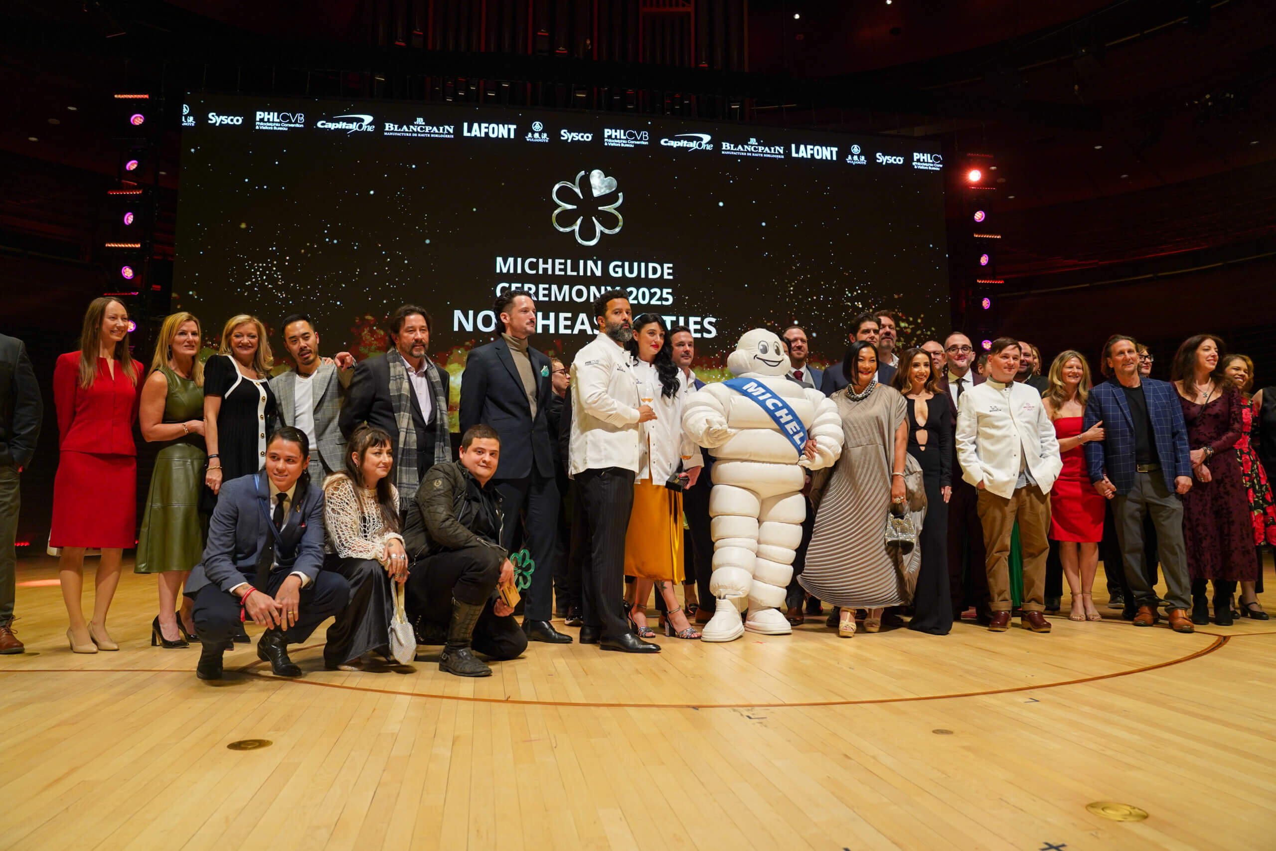 The Michelin mascot poses with a large group including newly starred Michelin chefs and other honorees.